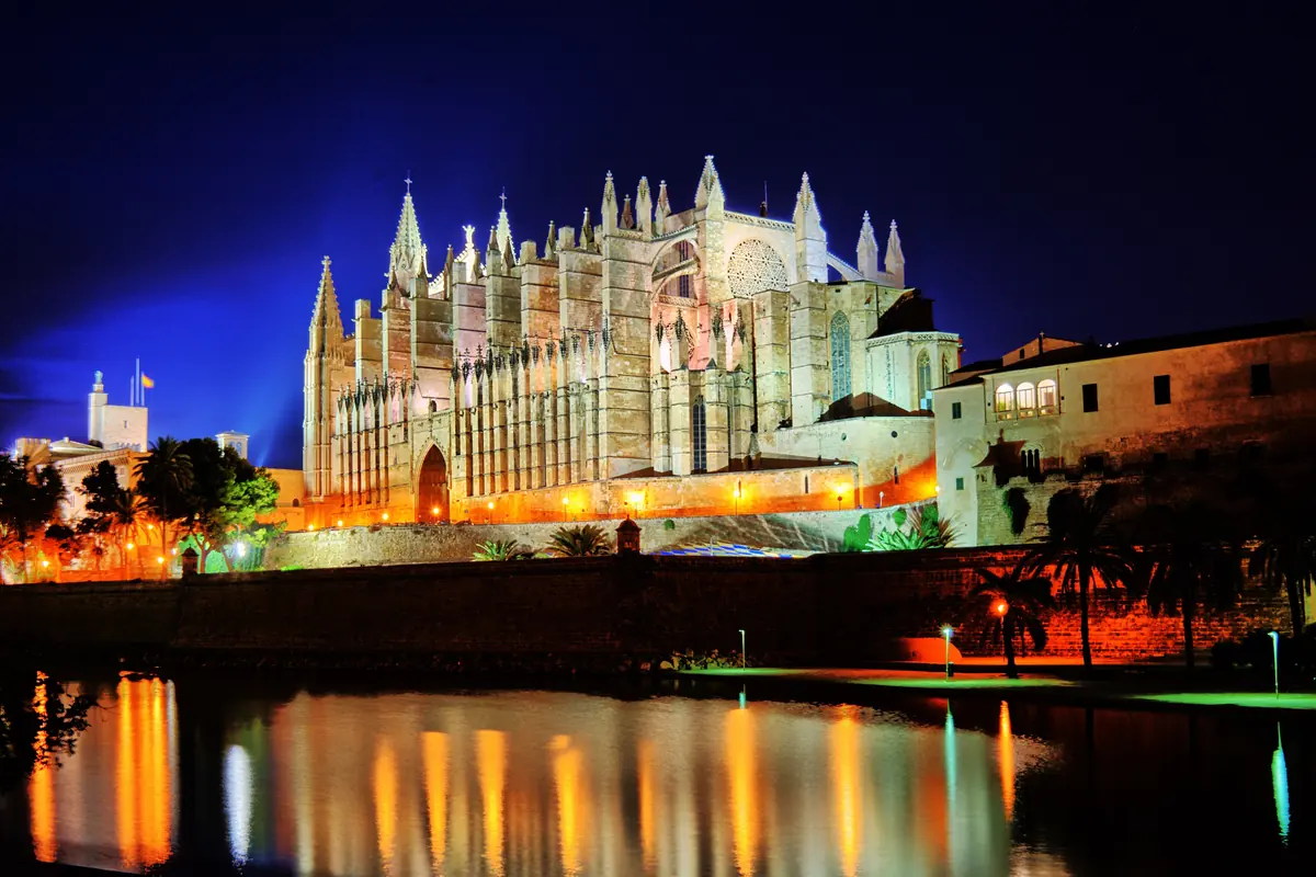 Palma Cathedral lit up against a deep blue night sky, reflected in the water in front of it